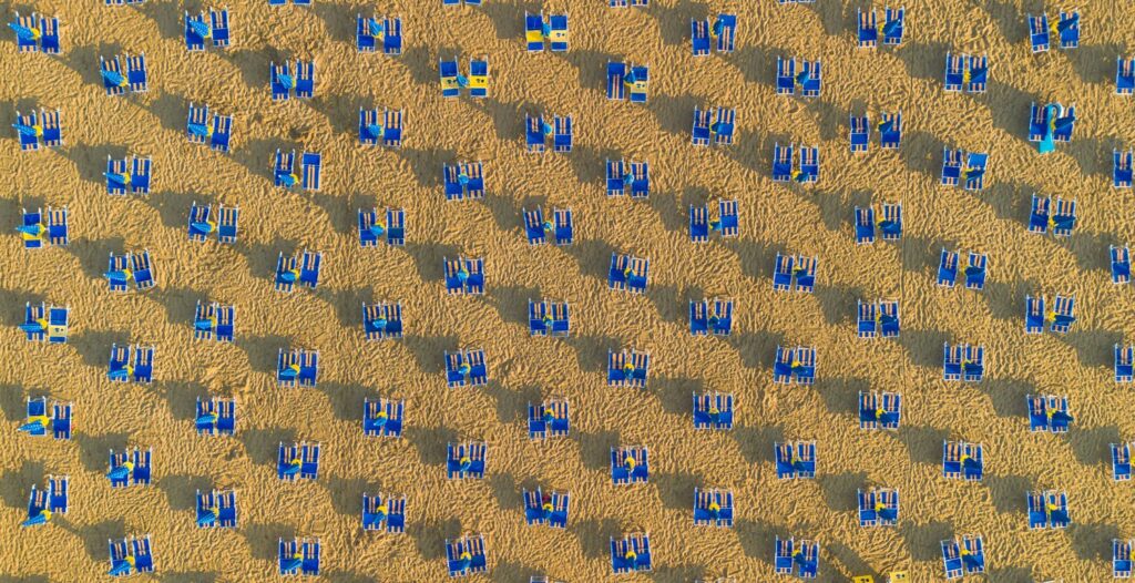 Blauwe ligbedden in een strak patroon op het strand van Lido di Jesolo van bovenaf